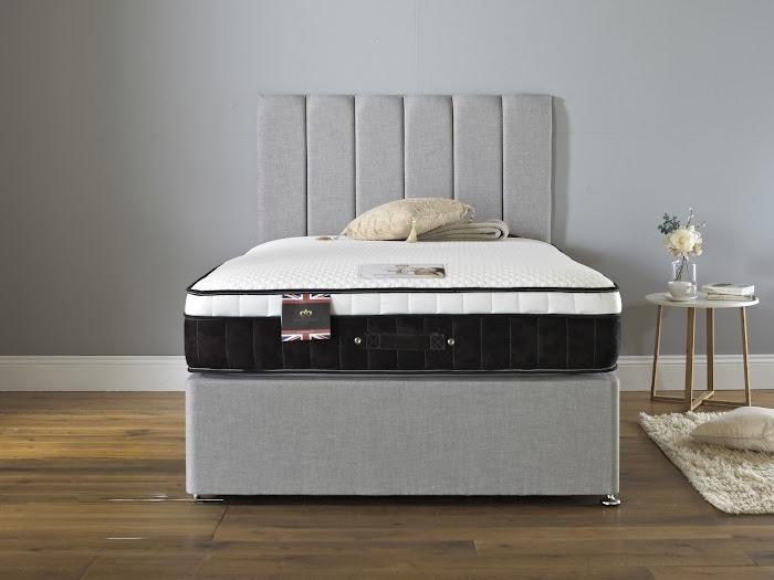 Gray upholstered bed with a mattress in a room with a gray wall and wooden floor.